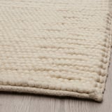 Textured, beige woven rug on a wooden floor. Intricate patterns and high-quality craftsmanship.
