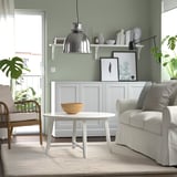 Living room with green walls, white coffee table, chairs, rug, and decorated shelf.