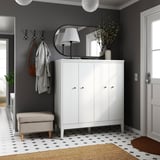 Modern entryway with IDANÄS white cabinet, round mirror, hanging coats, lamp, plant, checkered floor, and rug.