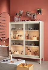 White IDÅSEN cabinet with glass doors displays sunglasses and decor against red wall.