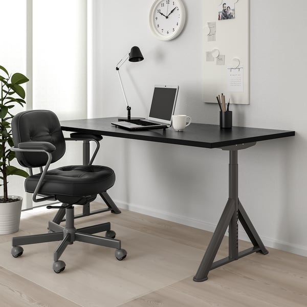 IDÅSEN desk & chair setup with cable net, laptop, mug & lamp. Whiteboard & clock in background.