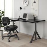 IDÅSEN desk & chair setup with cable net, laptop, mug & lamp. Whiteboard & clock in background.