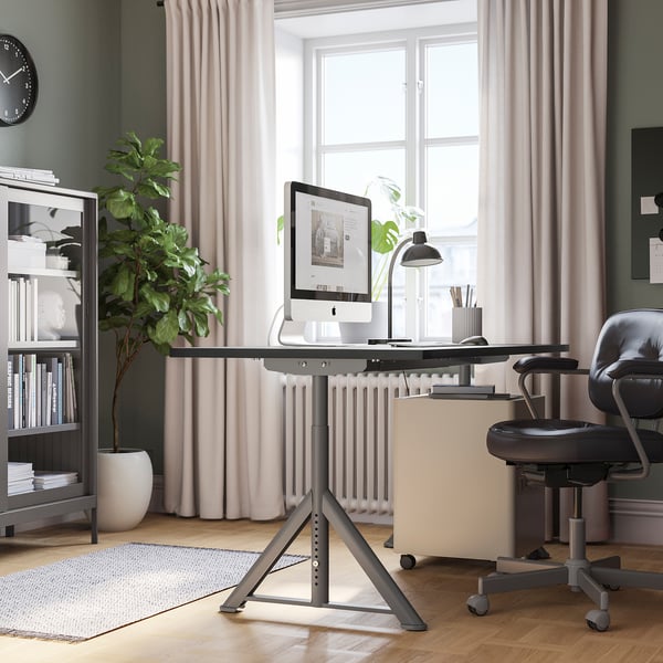 Modern home office with IDÅSEN desk, black chair, and bookshelf. Large window, adjustable desk, cable net, plants, and rug.
