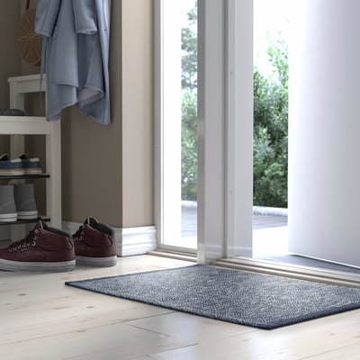 Dark blue IDROTTSPLATS mat near door, cotton, absorbent, complements flooring.