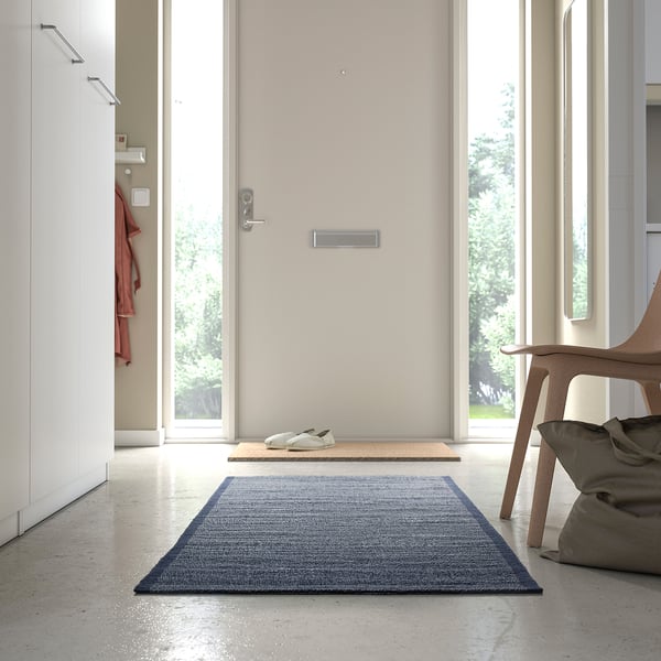 A modern entryway with a blue cotton rug, wooden chair, and red jacket hook.
