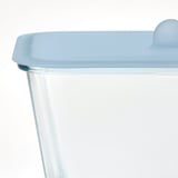 Close-up of a clear glass container with a blue silicone lid, designed for food storage and oven use. The lid a lip for easy handling.