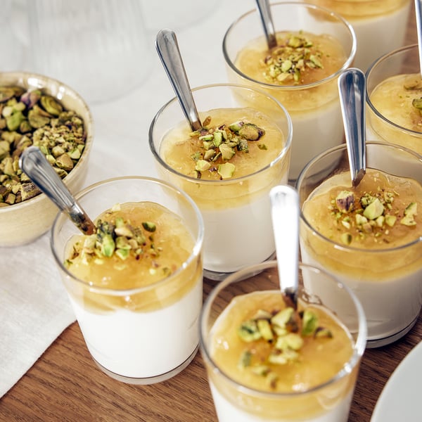 Small glasses filled with dessert topped with pistachios and spoons; perfect for serving desserts.