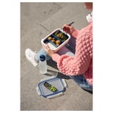 Person in pink sweater holds a divided pink lunchbox with colorful food. Beside them, another empty divided container rests on the ground.