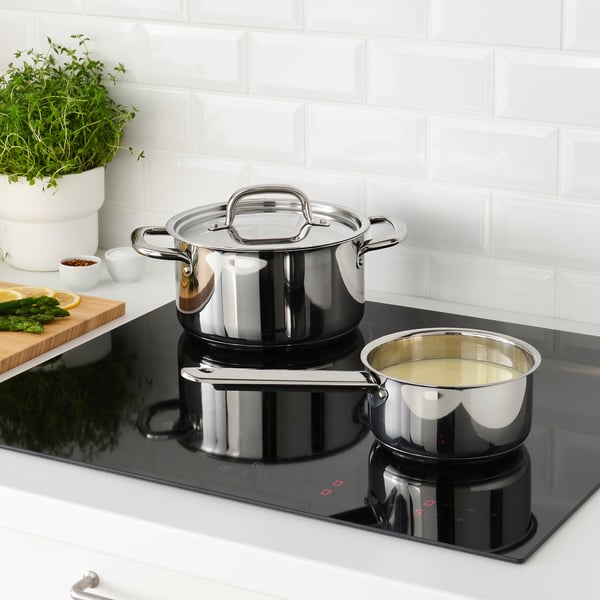 Stainless steel saucepan set on black induction cooktop, with one containing liquid, demonstrating heat-resistant handles and even heat distribution.