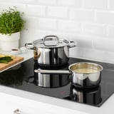 Stainless steel saucepan set on black induction cooktop, with one containing liquid, demonstrating heat-resistant handles and even heat distribution.