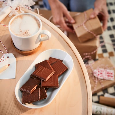 Cozy setup: oval plate with chocolate, coffee mug on wooden tray. Or, for fewer characters: chocolate, coffee on wooden tray.
