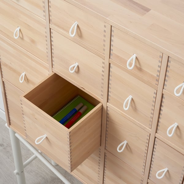 Light wooden drawers with white rope handles, one open displaying green pen holder with pens.
