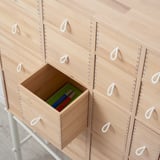 Light wooden drawers with white rope handles, one open displaying green pen holder with pens.