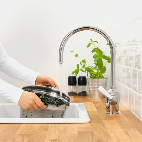 Person washing greens in sink. Modern chrome faucet with sensor turns water on and off with hand movement. Plants and spices nearby.
