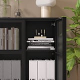 Black IVAR cabinet with shelves holding books and decor, anchored.