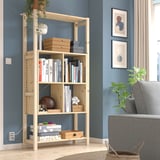 IVAR light pine bookcase stands tall near a blue wall, filled with books and boxes. Near a gray chair, its large and sleek.