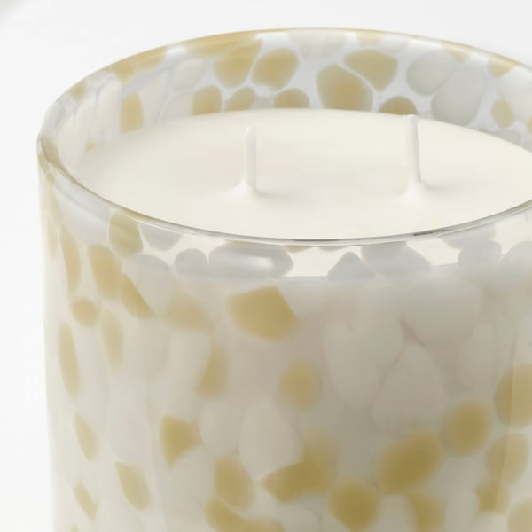 Candle in glass with yellow-white speckled design, smooth wax surface, three wicks.