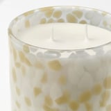 Candle in glass with yellow-white speckled design, smooth wax surface, three wicks.