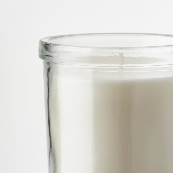 Glass container of JÄMLIK candle, with smooth edges, filled with creamy white wax, emitting a sweet vanilla scent.