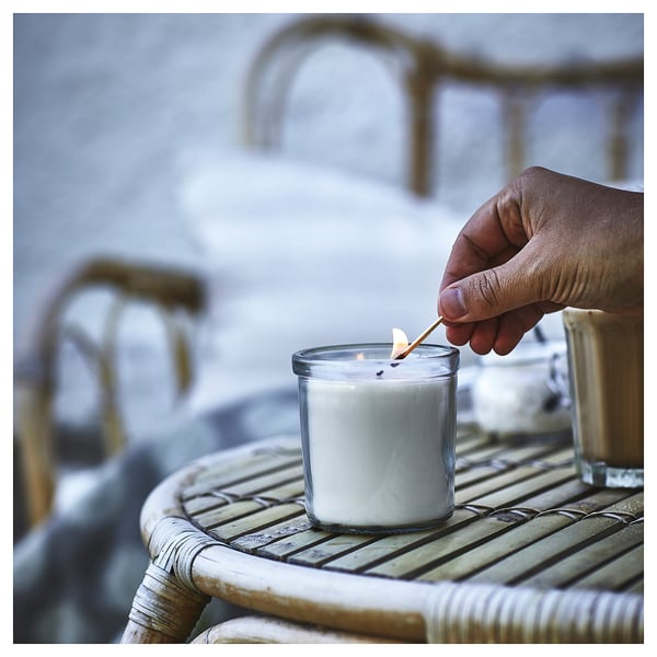 Hand lighting JÄMLIK scented candle on wicker table.