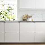 Modern kitchen: white JÄRSTORP, marble backsplash, sleek cabinets, minimal decor, utensils on grey counter, potted plant.