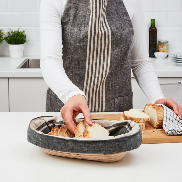 A person in an apron places bread into a round, woven JÄSNING proofing basket lined with cloth, showcasing its use in bread baking.