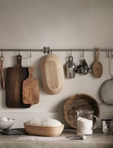 Kitchen wall with hanging tools: boards, sifter, peelers, basket, utensils, cups. Rustic design.