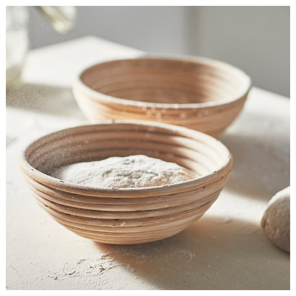 Two round woven bowls, one filled with flour. Light brown with a rustic design. On a marble surface.