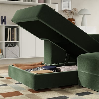 Green sectional sofa with ottoman, showing open storage for blankets, books, and remote controls beneath seat.