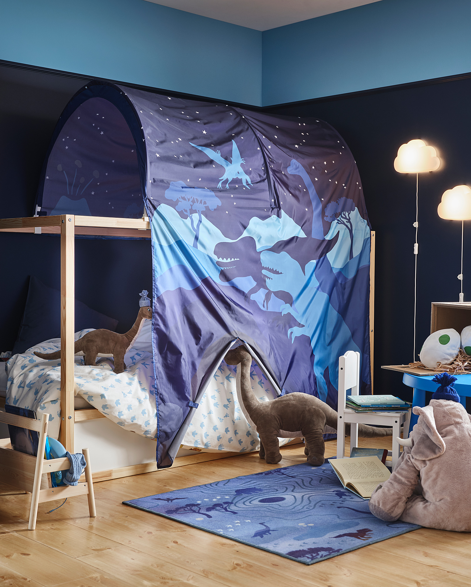 Kids dinosaur-themed room a blue and gray tent over a bunk bed, dinosaur soft toys, and a rug with a dinosaur design.