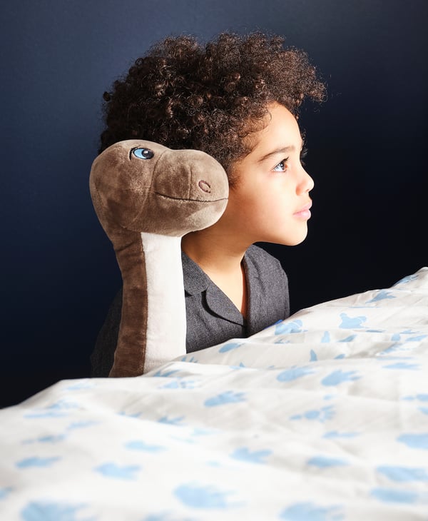 Girl on bed with dinosaur pillow, thoughtful.