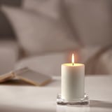 White JUBLA candle in glass holder burns brightly. Small, clean design.