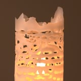 A white, perforated candle emits a warm glow, revealing intricate patterns as it burns.
