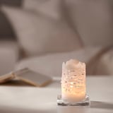 JUBLA: white lace candle on clear base, small, on white surface.