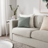 Living room with green, eco-friendly KÄRLEKSGRÄS cushion on light sofa.
