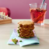Stack of ginger cookies on blue napkin, glass of red drink, wooden toy behind.