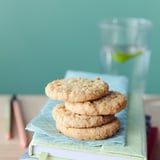 Stack of four oat cookies on blue napkin, glass, light green wall.