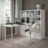 Modern minimalist home office with white KALLAX shelf unit, desk, and chair. Large window with sheer curtains, wooden floor.