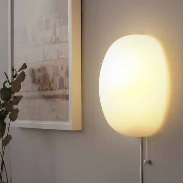 Wall-mounted glass lamp with soft, diffused light beside a framed picture.