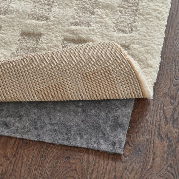 Rug with felt backing and beige textured surface placed on wood floor.