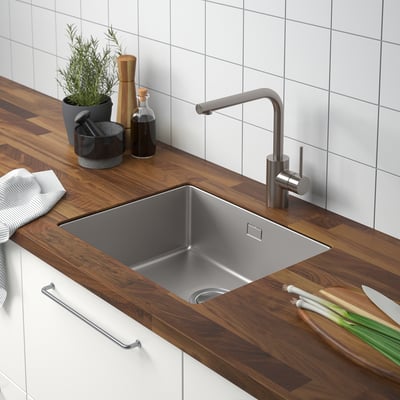 Modern kitchen with stainless sink, onions, towel, plant.