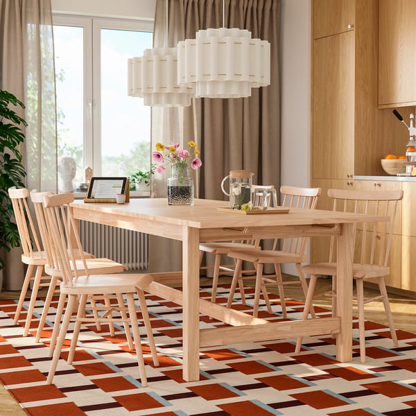 KARSKÄR dining set with light wood table, six spindle chairs, modern chandelier, translucent seats, large windows, vibrant rug.
