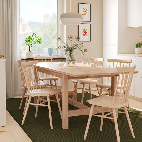 Modern KARSKÄR dining setup with extendable table and six spindle chairs. Decor includes vase with flowers and wall art, next to kitchen.