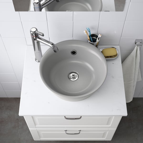 A modern marble sink with chrome faucet on quartz countertop, toothbrush holder, and soap dish.