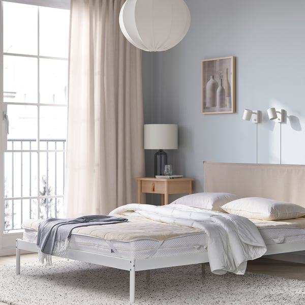 Modern bedroom with blue bed, bedside table, lamp, vase, window, art.