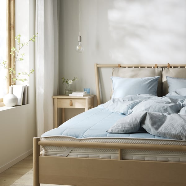 Cosy bedroom with wooden bed, blue bedding, bedside table with flowers, and hanging light.