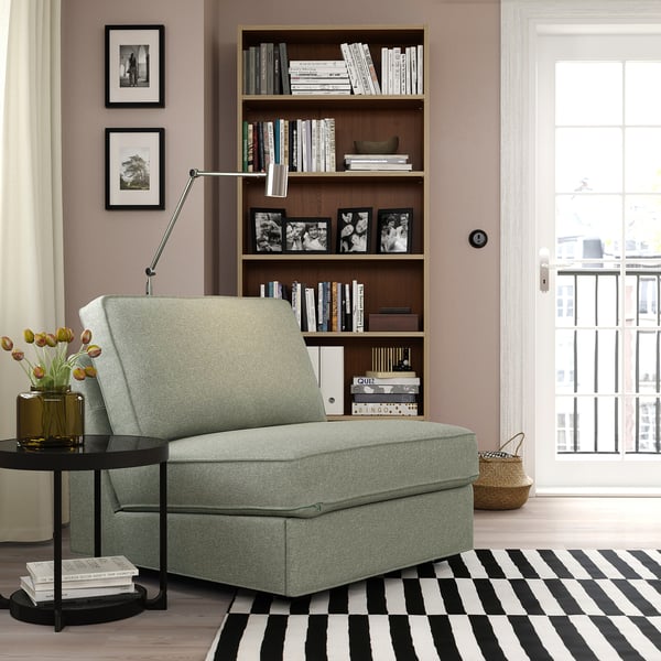 Modern living room with KIVIK green sofa-bed, striped rug, black side table, bookshelf, and large window.