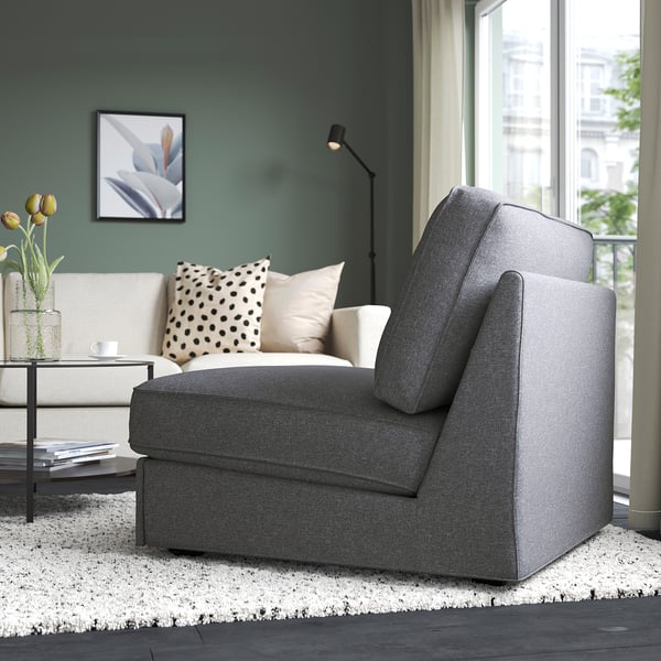 Modern living room with grey sofa-bed, white rug, coffee table with books, flowers, and polka dot pillow. Large window shows city view.