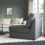 Modern living room with grey sofa-bed, white rug, coffee table with books, flowers, and polka dot pillow. Large window shows city view.
