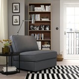 Modern grey KIVIK sofa-bed near bookcase, black & white rug, black side table with flowers, window.